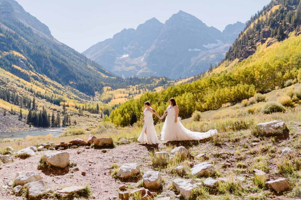 Two brides walk hand in hand at the Maroon Bells Amphitheater during their wedding in the fall