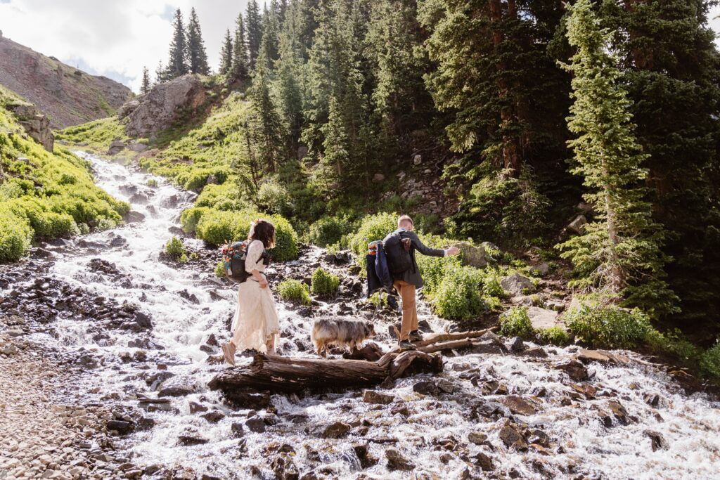 Couple hikes across a river at Blue Lakes in Colorado for their wedding