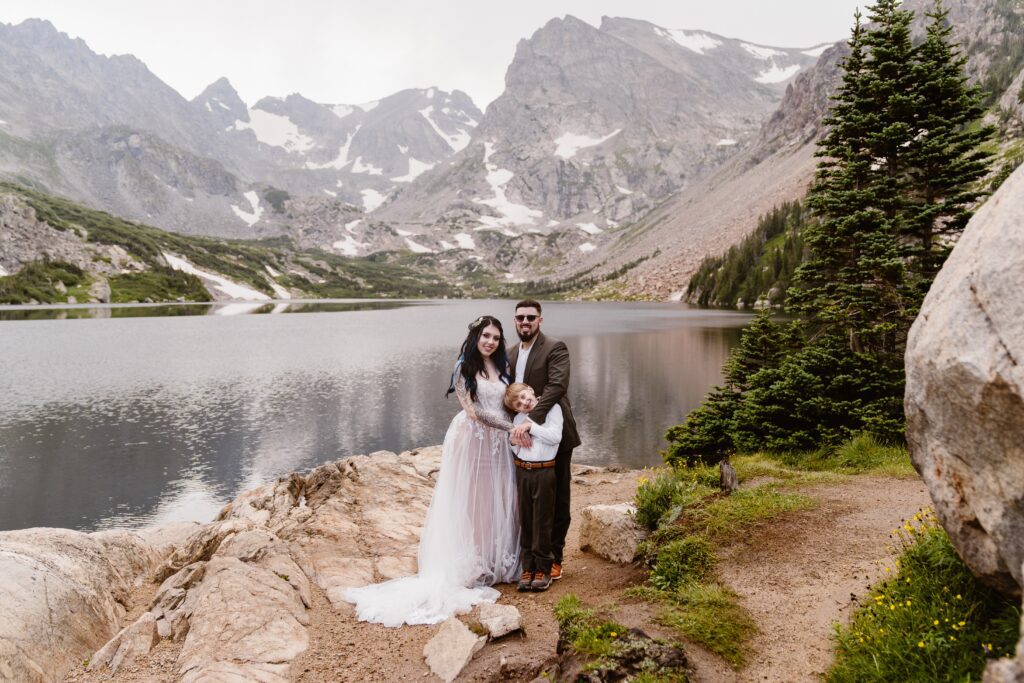 family stands together a an alpine lake in colorado