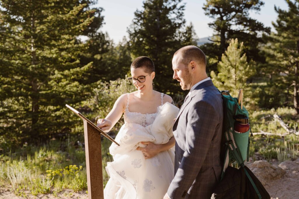 Bride and groom smile while reading a trail sign during their Estes Park, Colorado elopement.

