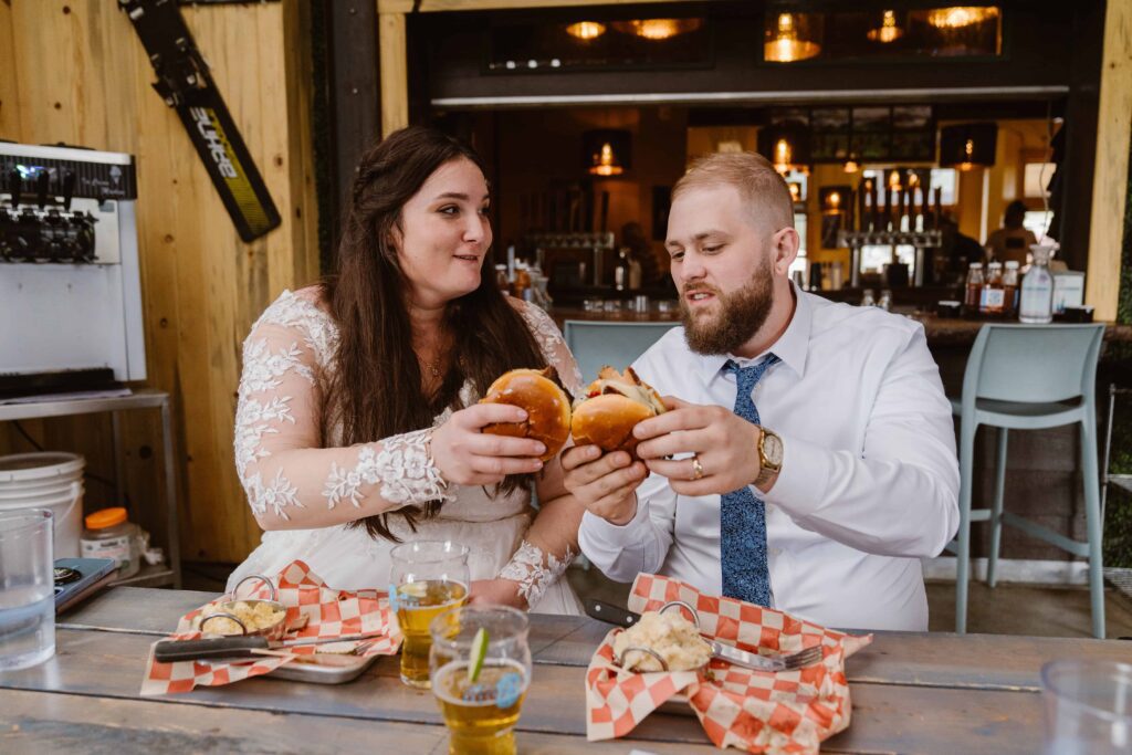 Bride and groom in wedding attire sharing burgers and beers at a laid-back bar in Black Hawk Colorado after their elopement