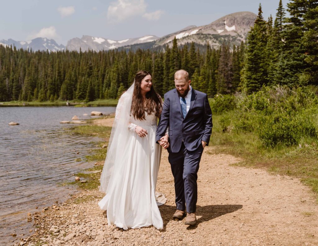 Bride and groom walking hand in hand along the lakeshore surrounded by pine trees at their Brainard Lake elopement