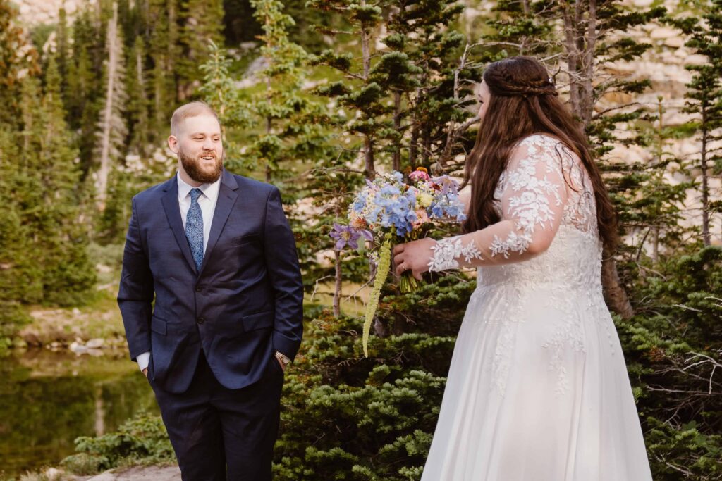 Groom smiling at bride holding her bouquet after seeing her for the first time