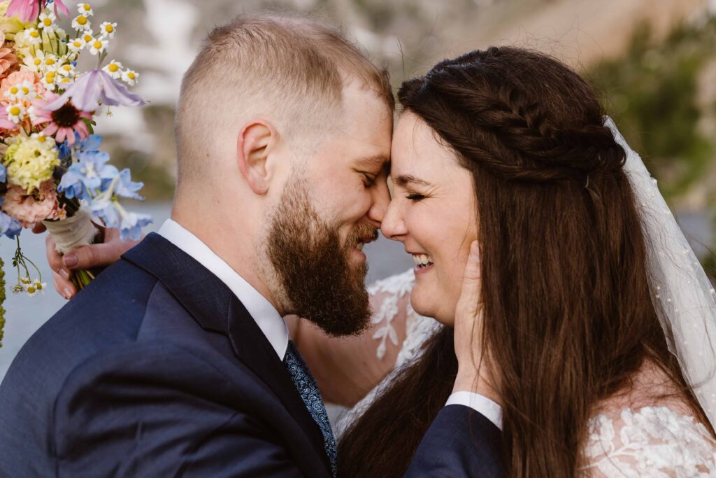 Bride and groom smiling with foreheads together holding a wildflower bouquet during their Lake Isabelle elopement