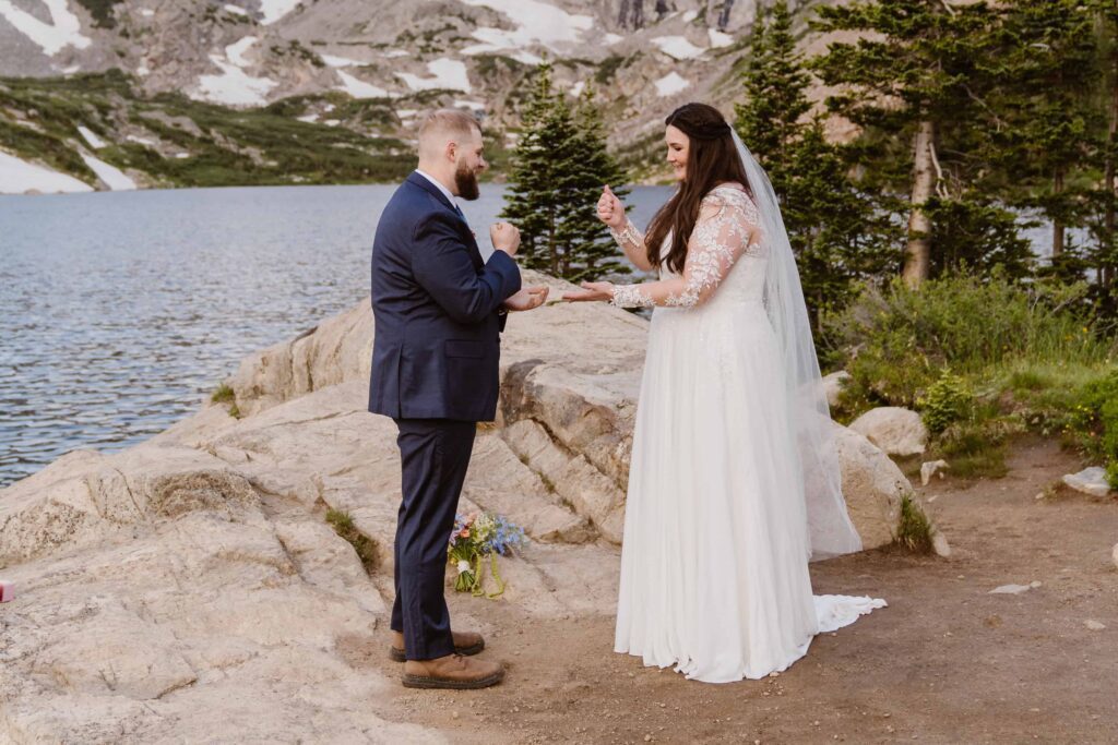 Bride and groom playing rock paper scissors on the rocky lakeshore before their ceremony