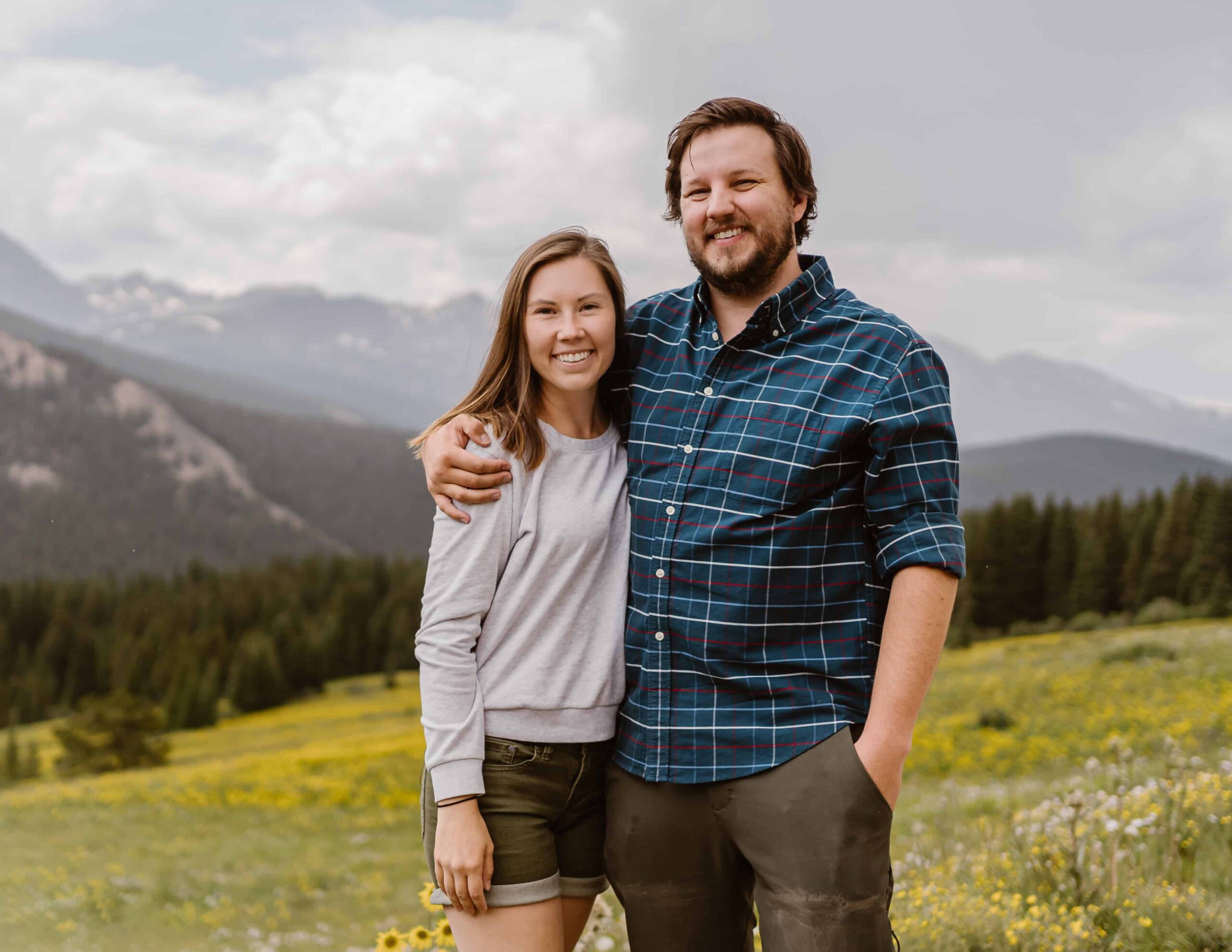 Casual outdoor portrait of a Colorado elopement photography and videography team in a wildflower meadow with Colorado mountains in the background.