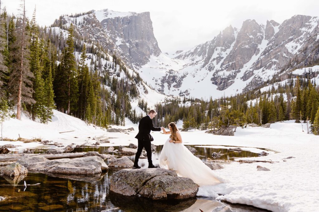 Groom helps bride up onto a rock at Dream Lake after their elopement at Sprague Lake in Rocky Mountain National Park