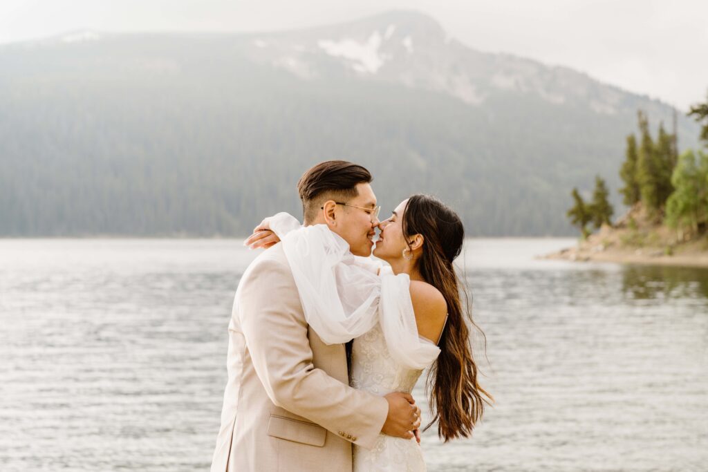 Newlyweds sharing a romantic kiss with misty Colorado mountains behind them at their Airbnb elopement.