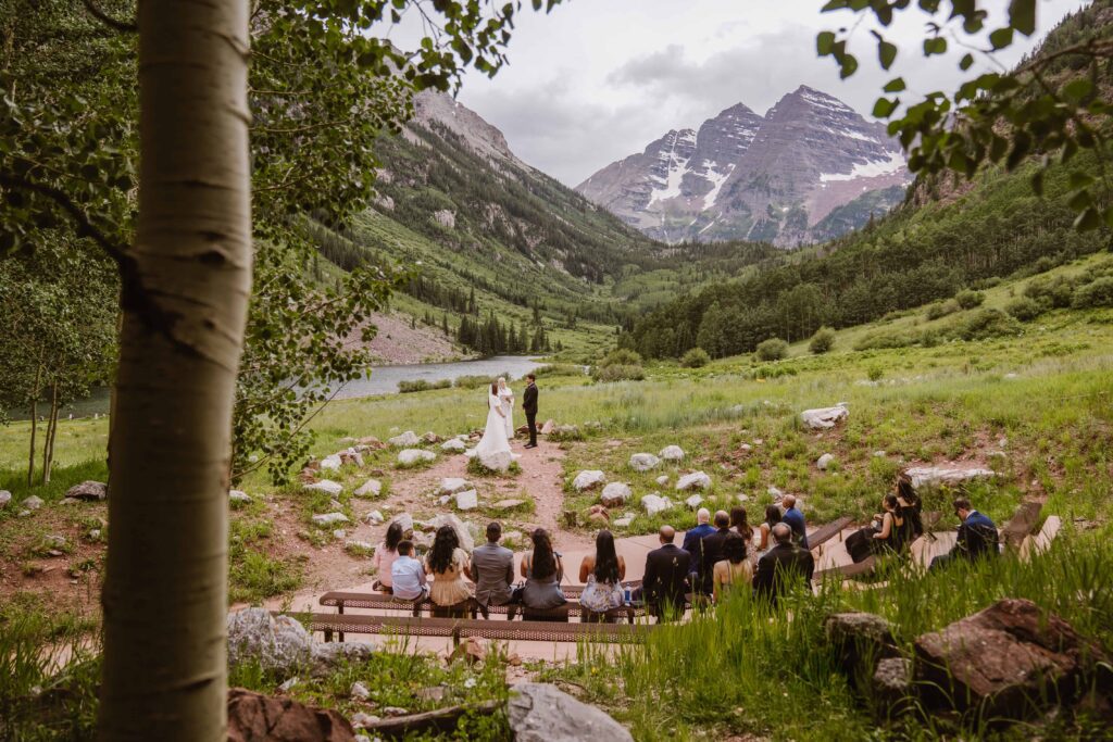 Wide view of a wedding ceremony at Maroon Bells Amphitheater with guests seated and mountain peaks rising in the background with Maroon Bells Amphitheater Elopement Photographer Alpine Vows